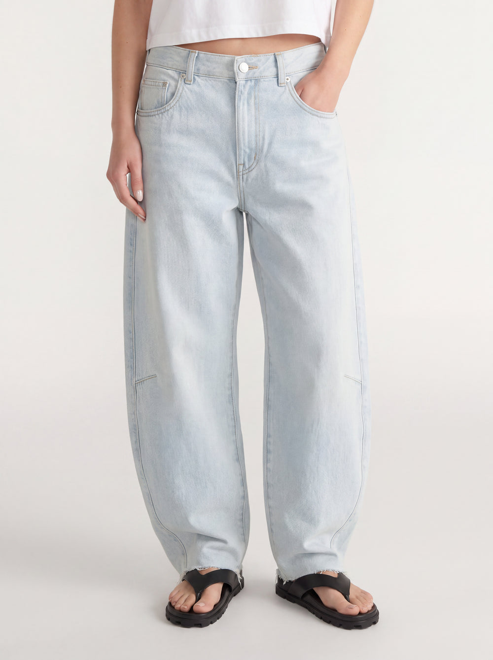 Woman wearing light wash barrel leg jeans with an adjustable waist and black sandals