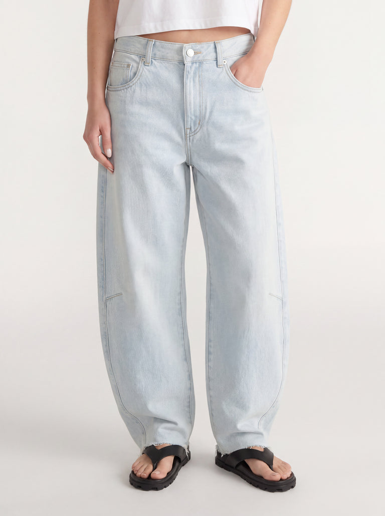 Woman wearing light wash barrel leg jeans with an adjustable waist and black sandals