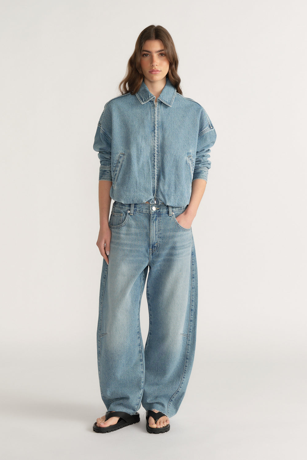 Woman wearing relaxed fit light wash denim jeans with a cinched waist paired with a loose denim jacket and black sandals