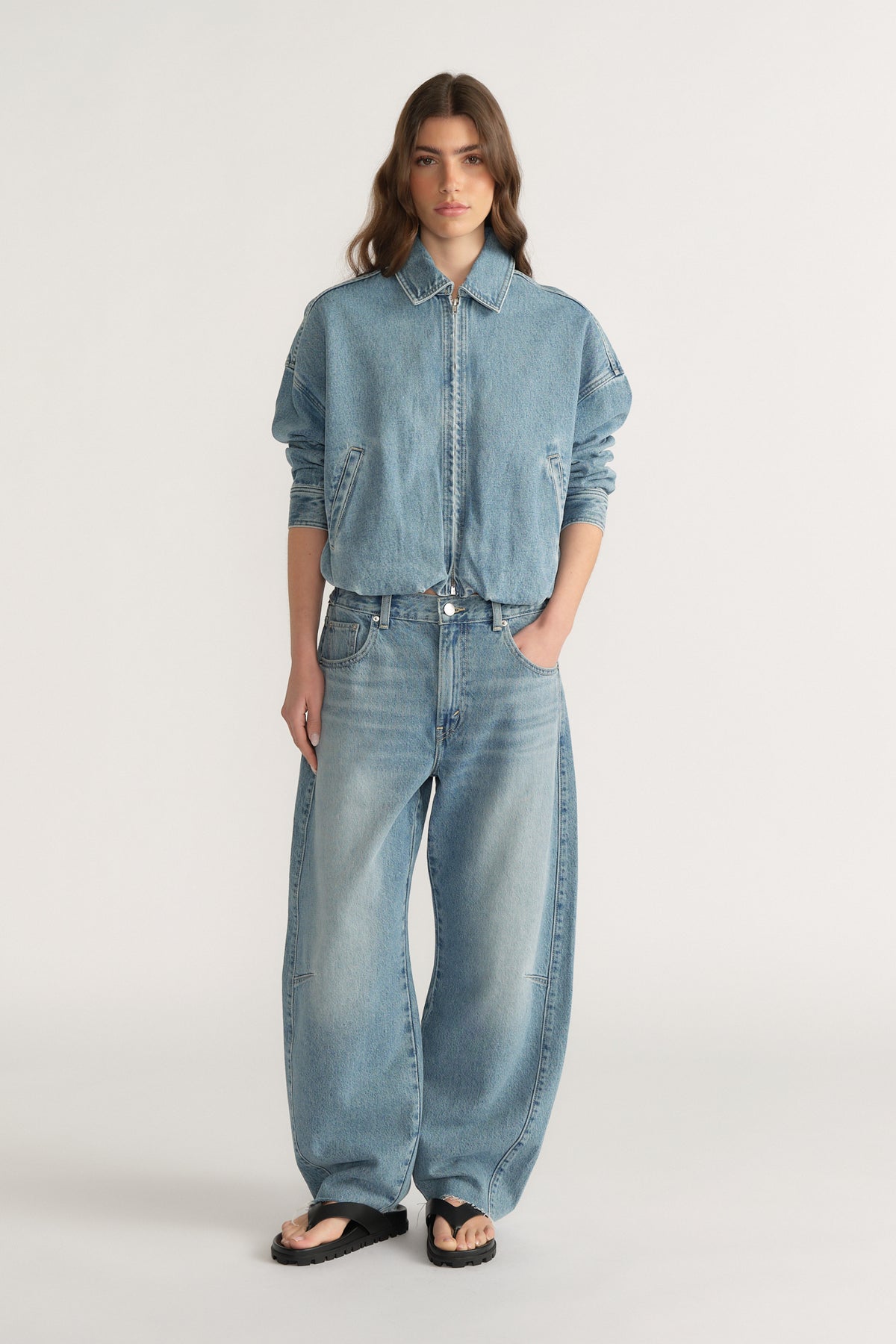 Woman wearing relaxed fit light wash denim jeans with a cinched waist paired with a loose denim jacket and black sandals