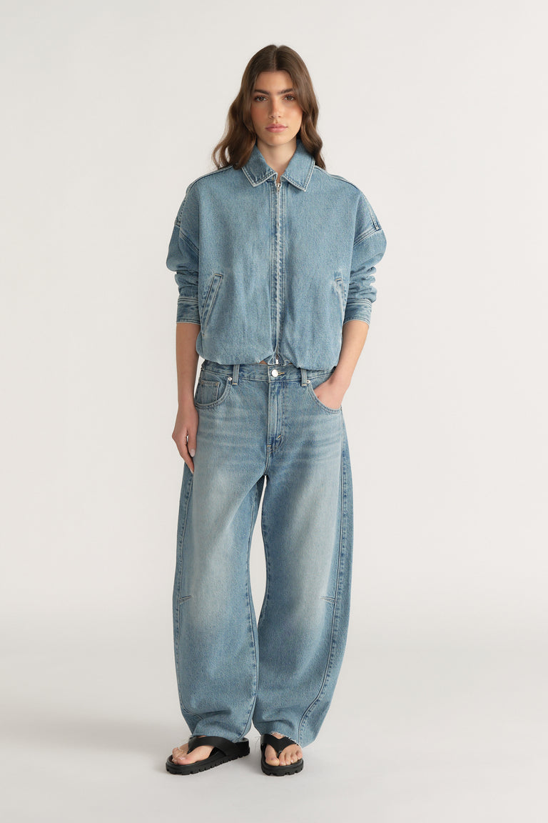 Woman wearing relaxed fit light wash denim jeans with a cinched waist paired with a loose denim jacket and black sandals
