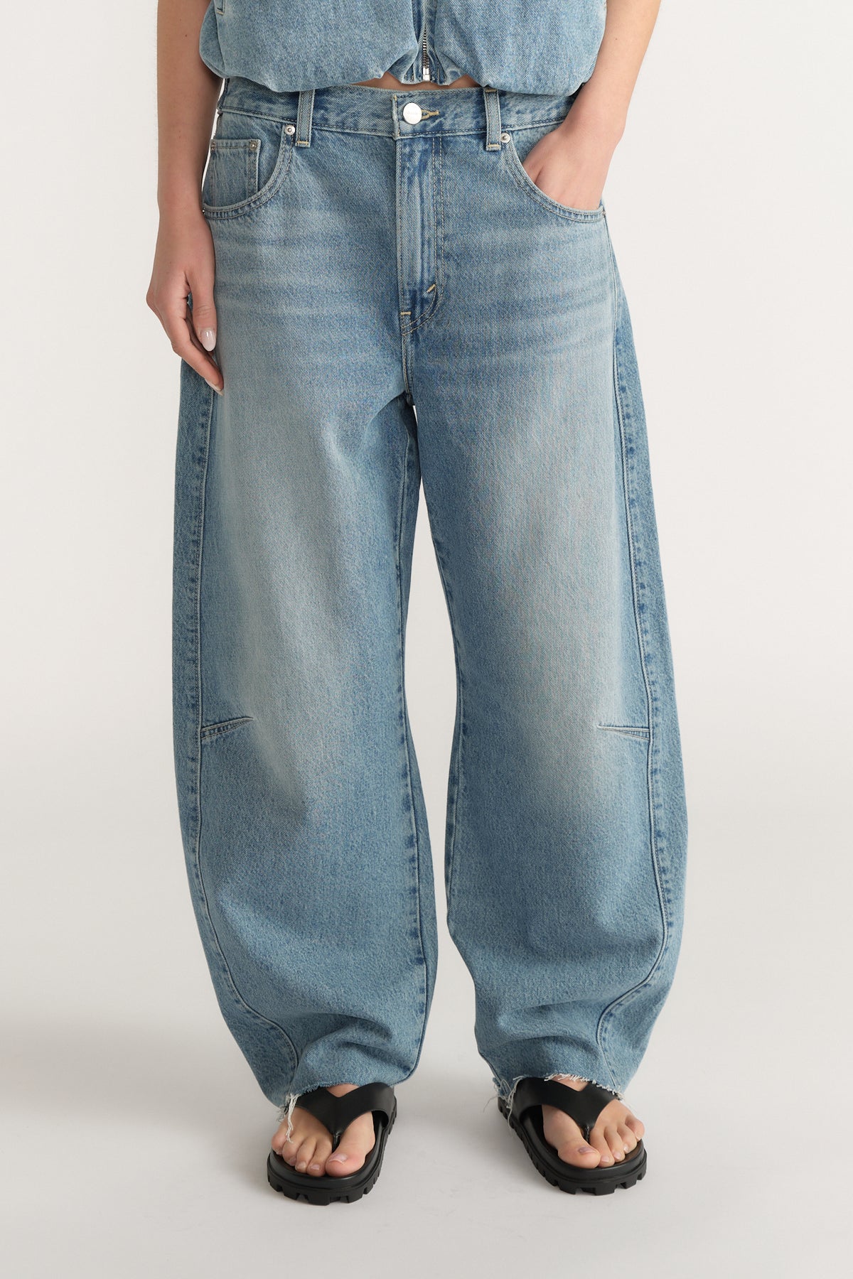 Front view of woman wearing light wash loose fit denim jeans with an adjustable waistband and black sandals