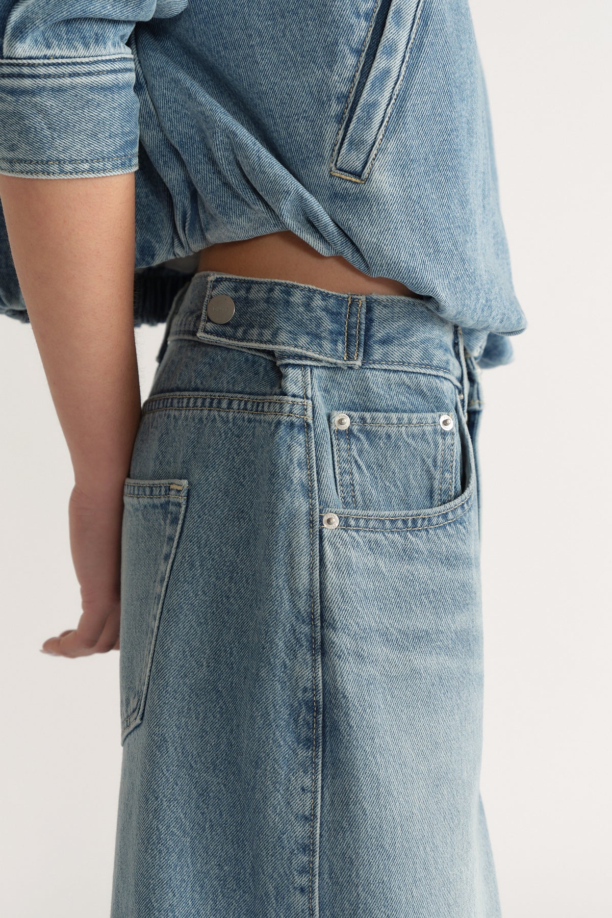 Side view of a woman wearing light wash high-rise denim jeans with a relaxed fit and rolled-up denim jacket sleeves