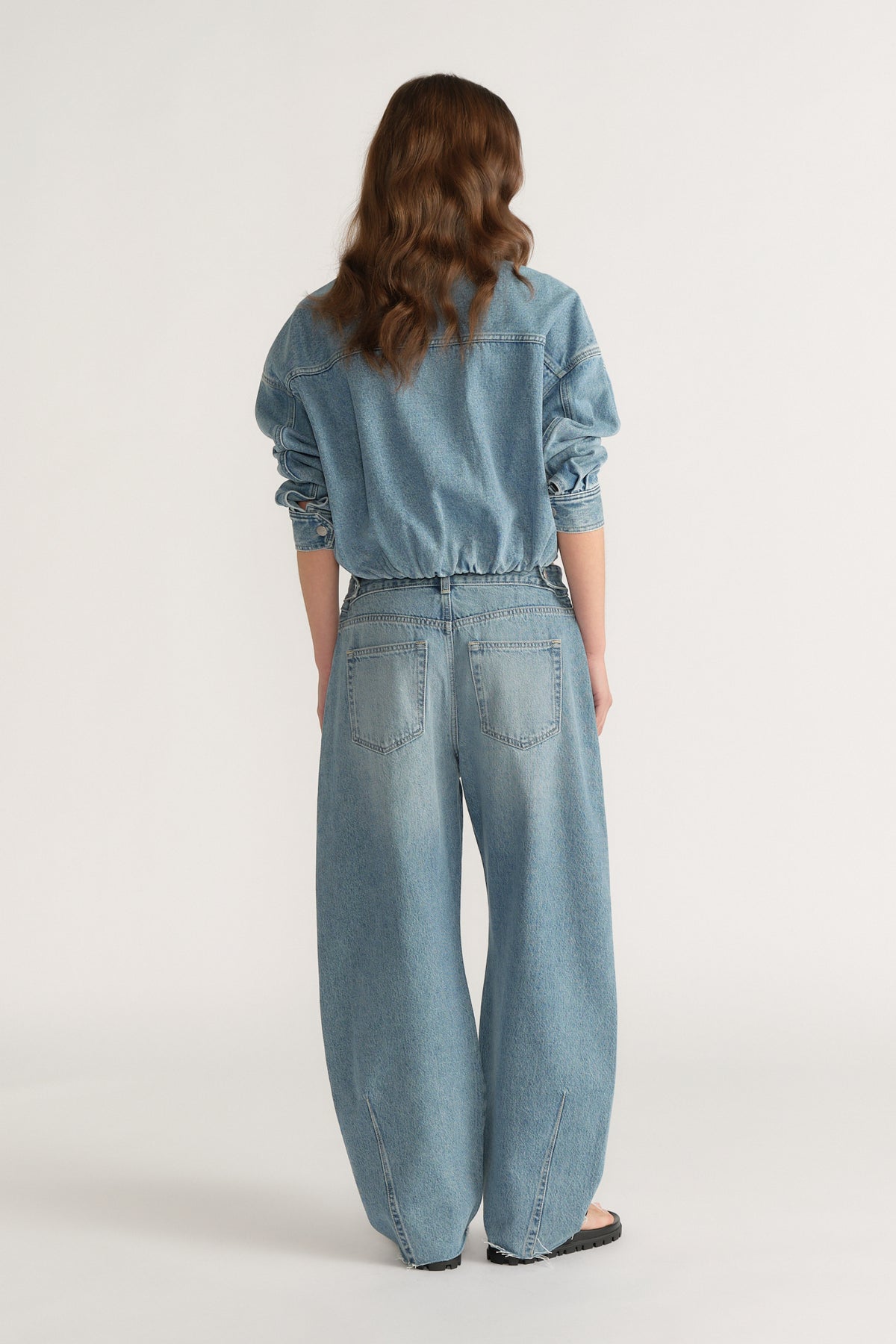 Rear view of woman wearing light blue wide-leg denim jeans with cinched waist and long sleeve denim top