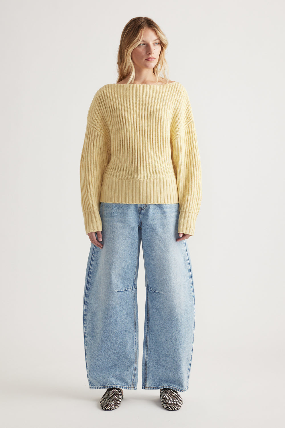 Woman wearing a soft yellow ribbed knit jumper with drop shoulders paired with wide-leg light blue denim jeans