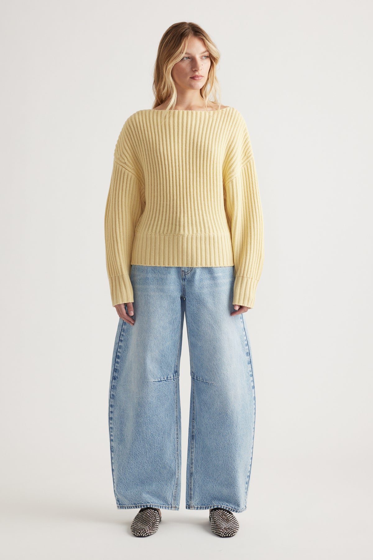 Woman wearing a soft yellow ribbed knit jumper with drop shoulders paired with wide-leg light blue denim jeans