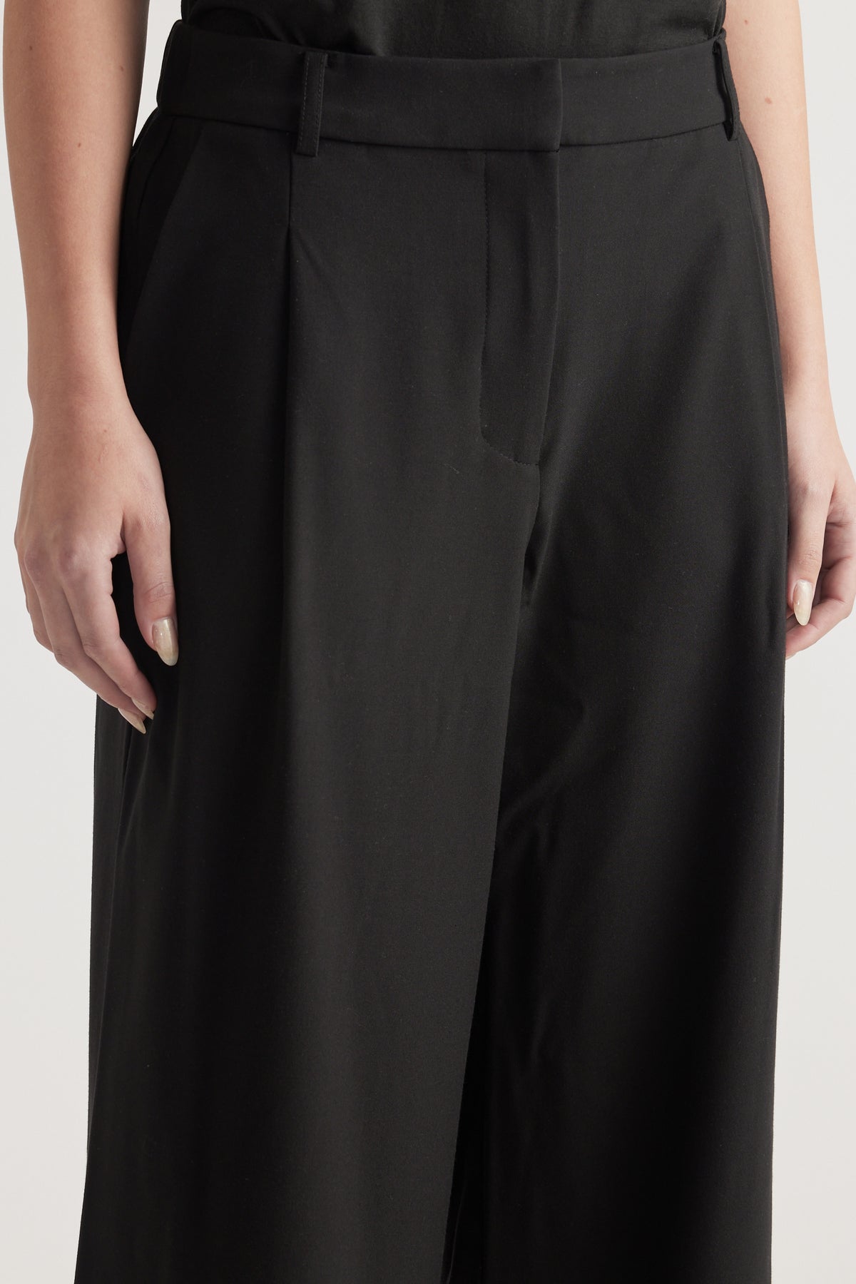 Close-up of woman wearing black high-rise tailored wide-leg pants with a pleated front