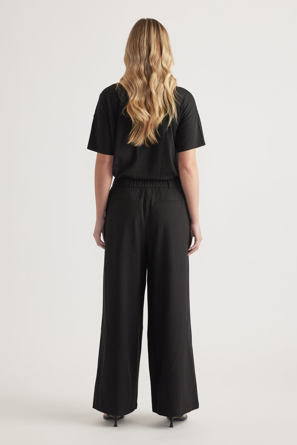 Back view of woman wearing high-rise black wide-leg tailored pants with a black top