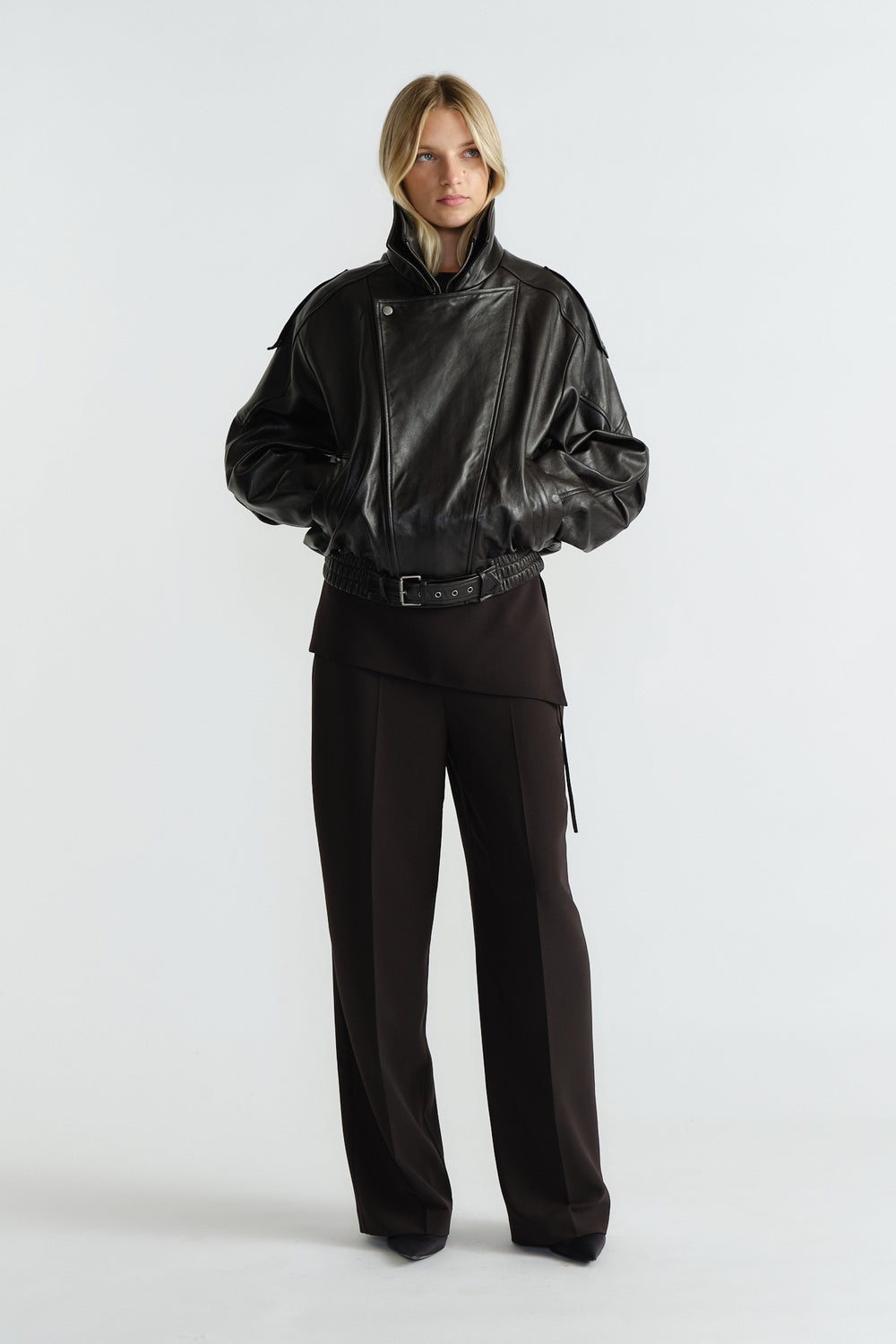 Woman wearing a structured black leather jacket paired with high-waisted, wide-leg tailored black pants.