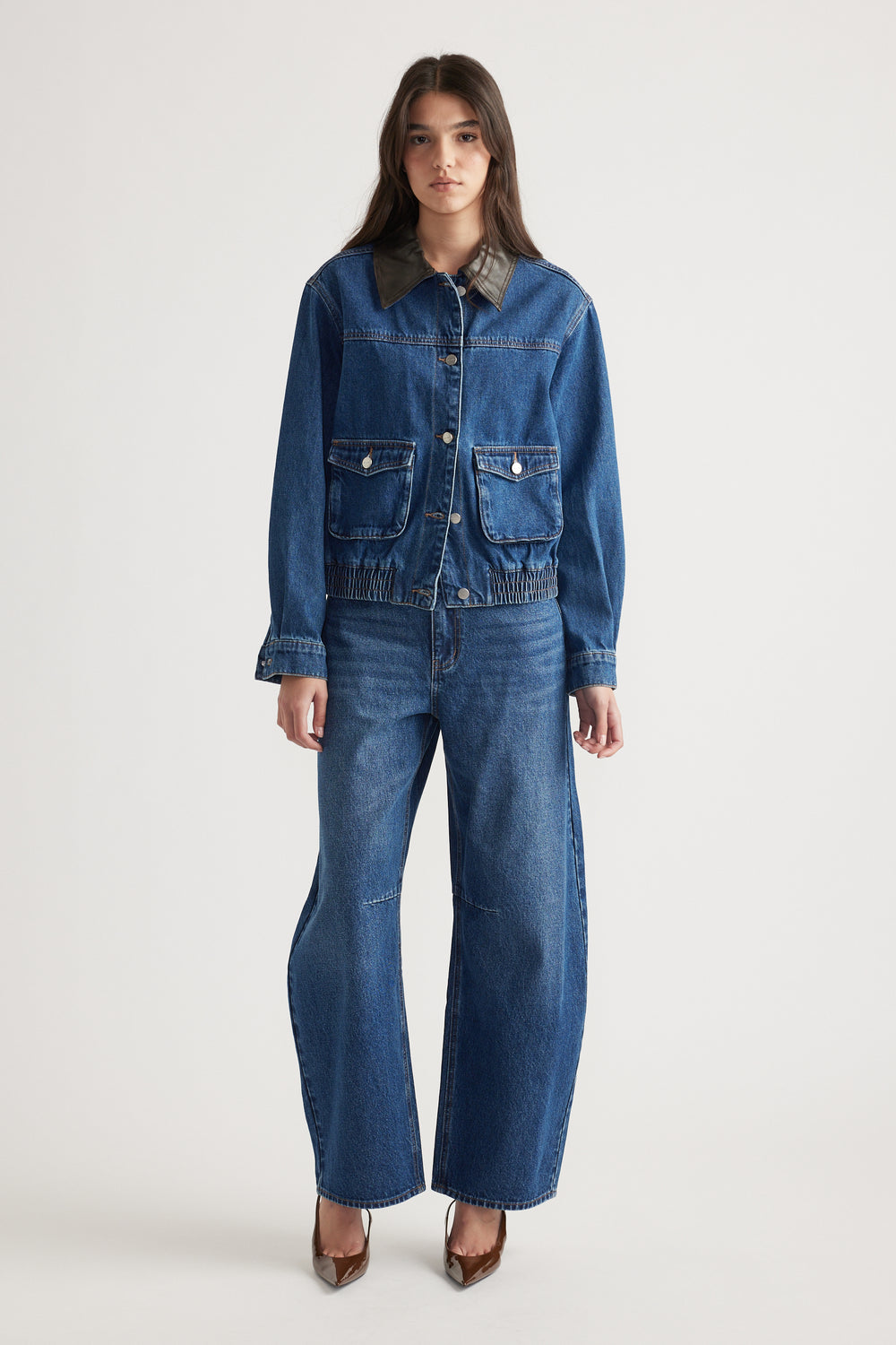 Young woman wearing a denim jacket with contrast collar and wide-leg jeans, styled with pointed brown heels.