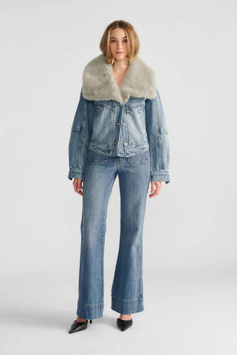 Woman wearing a light blue denim jacket with a plush fur collar paired with high-rise flared denim jeans and black shoes.