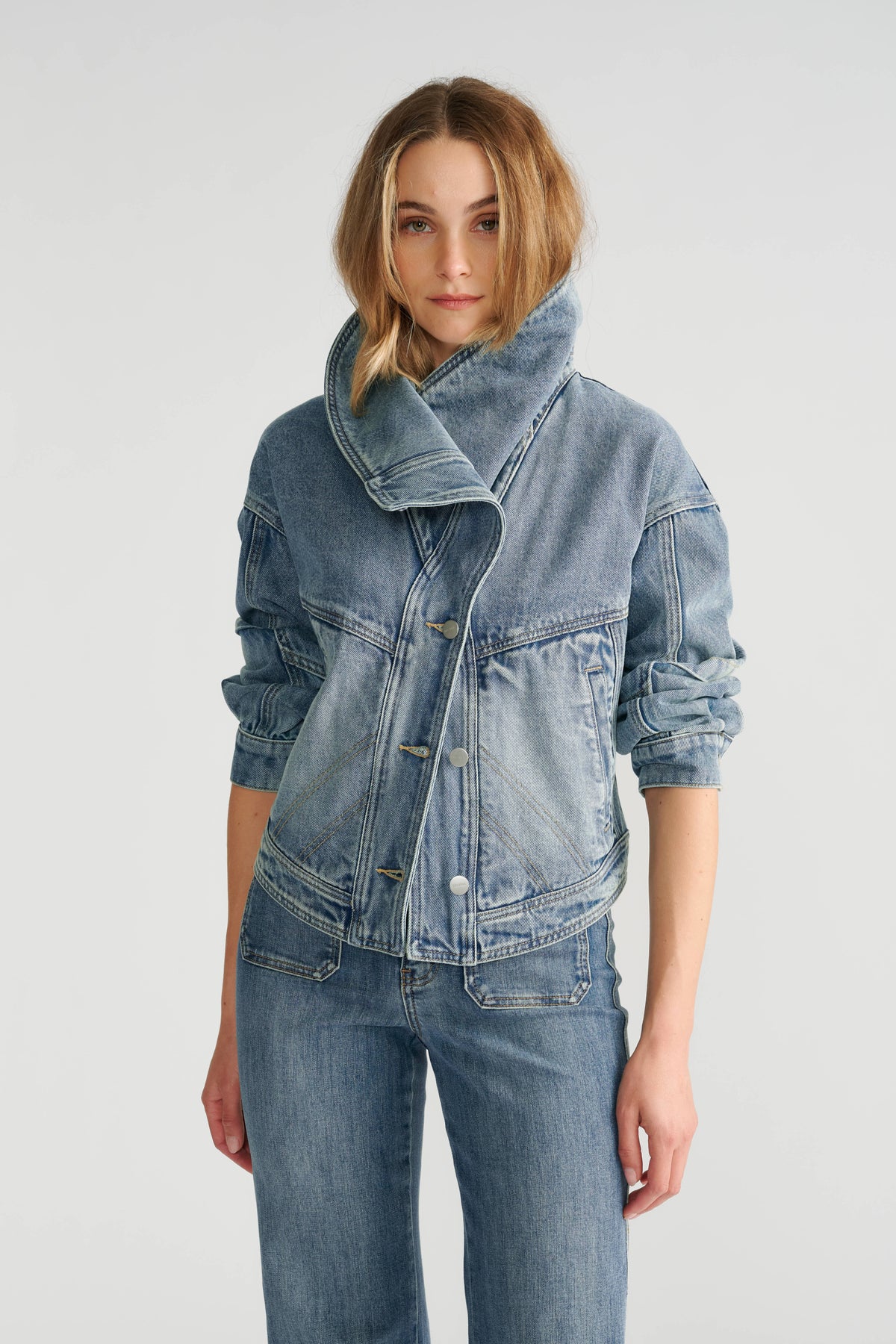 Woman wearing a light indigo denim jacket with a high fur collar paired with matching denim jeans.