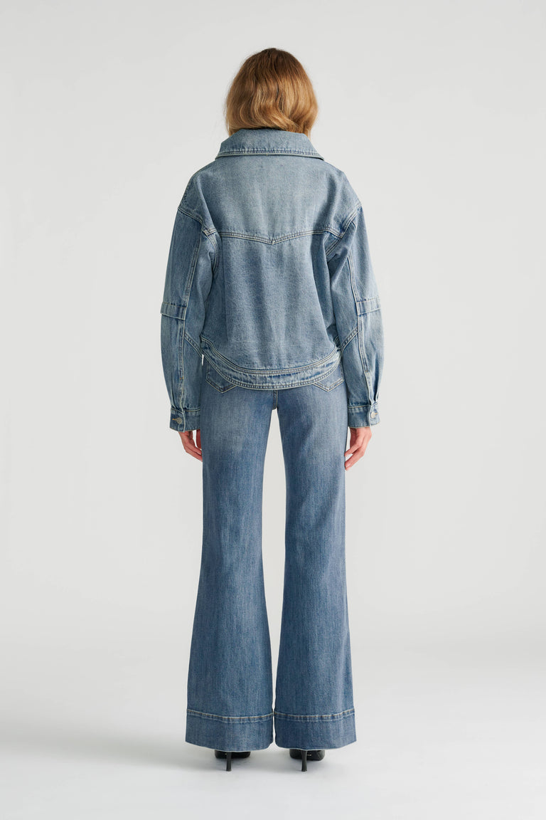 Woman wearing a light indigo denim jacket with a fur collar paired with high-rise wide-leg denim jeans and black heels.