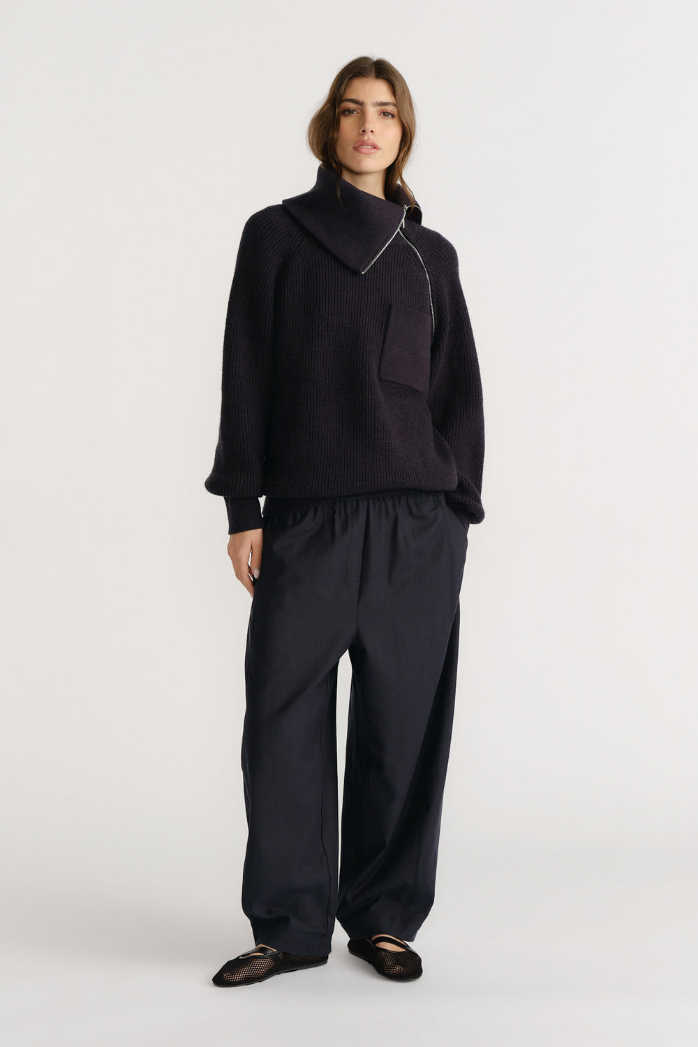 Woman wearing relaxed navy twill pants with a loose fit, paired with a cozy black knit sweater and ballet flats.