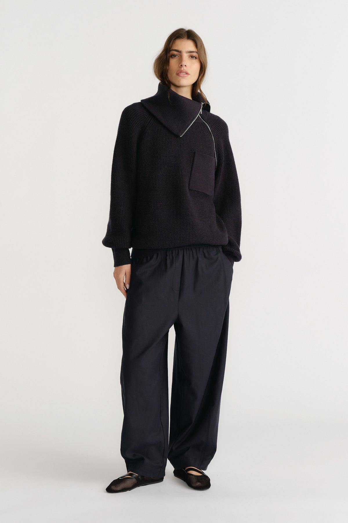 Woman wearing relaxed navy twill pants with a loose fit, paired with a cozy black knit sweater and ballet flats.