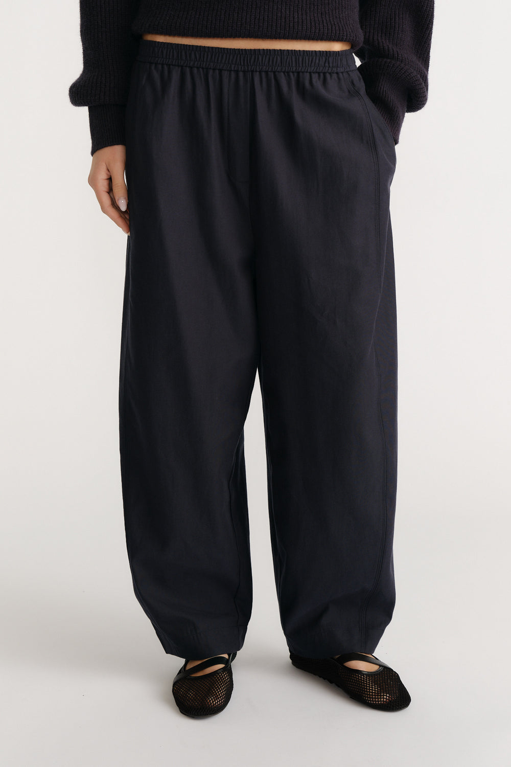 Relaxed navy wide-leg pants with elastic waistband paired with a black knit top and mesh ballet flats for casual style.