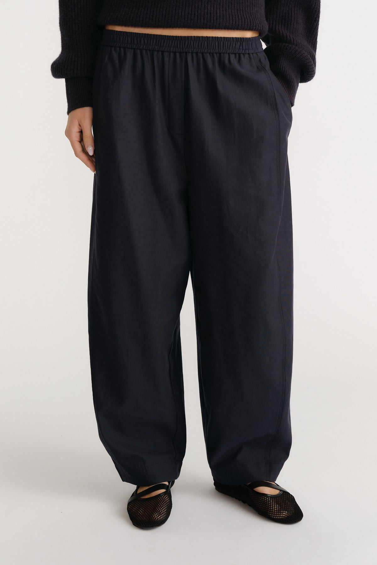 Relaxed navy wide-leg pants with elastic waistband paired with a black knit top and mesh ballet flats for casual style.