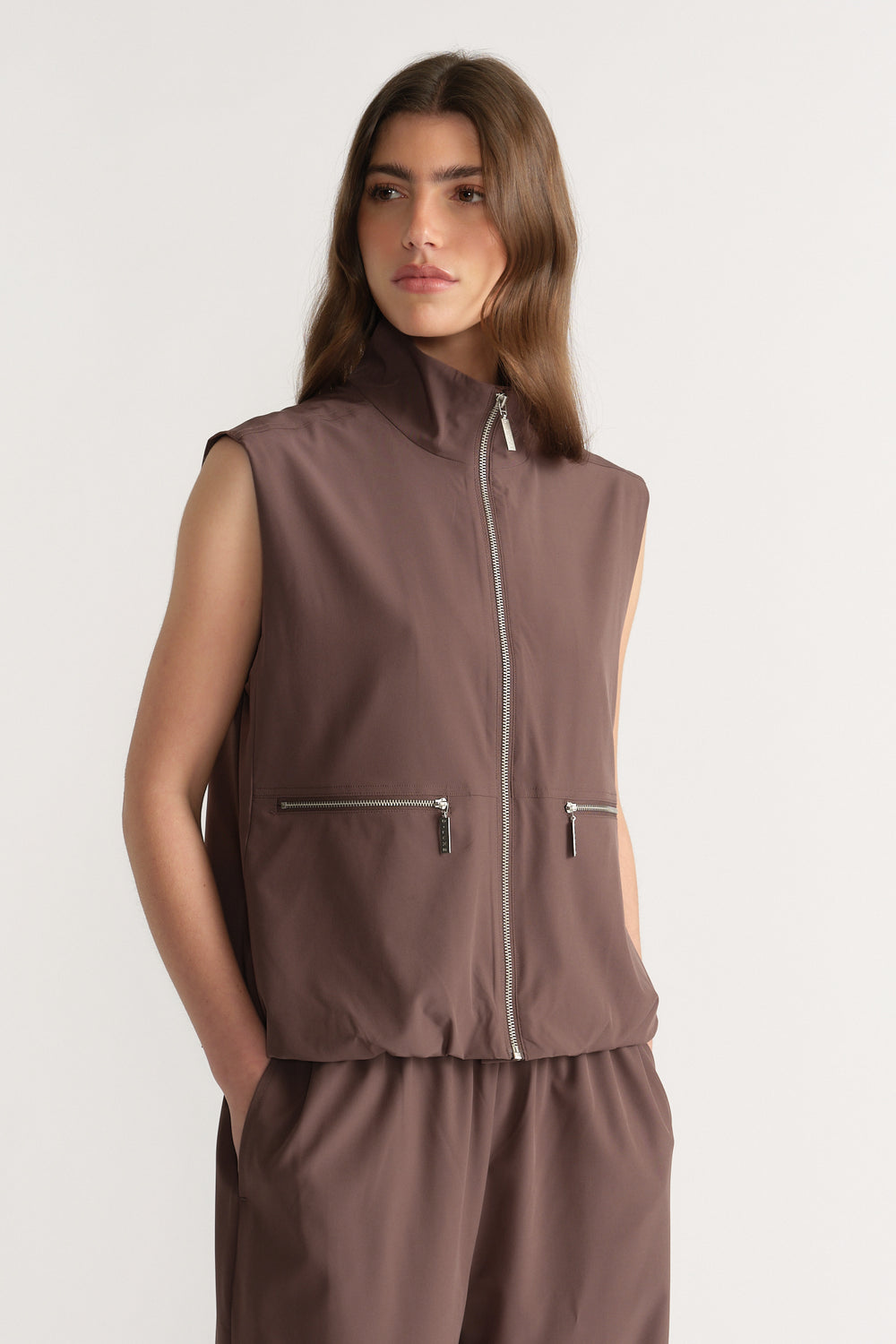 Woman wearing a brown sleeveless high neck gilet with front zip pockets and matching pants