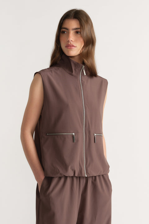 Woman wearing a brown sleeveless high neck gilet with front zip pockets and matching pants