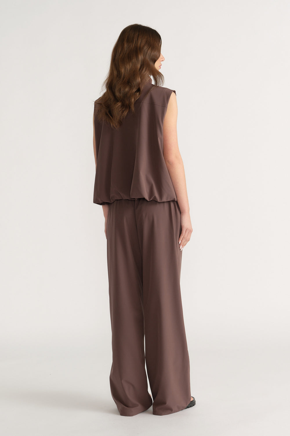 Back view of a woman wearing a brown sleeveless gilet with matching wide leg pants