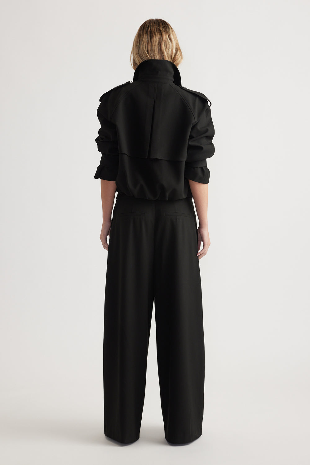 Rear view of woman wearing high-rise wide leg black pants paired with a black cropped jacket with rolled sleeves