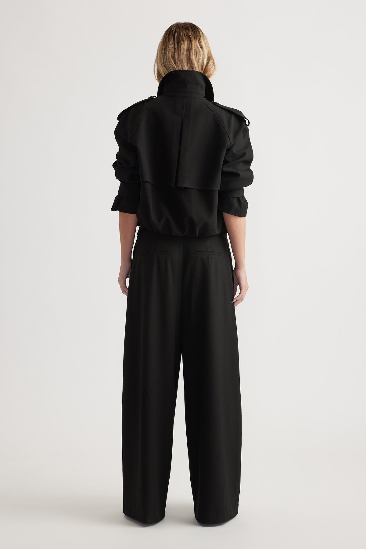 Rear view of woman wearing high-rise wide leg black pants paired with a black cropped jacket with rolled sleeves