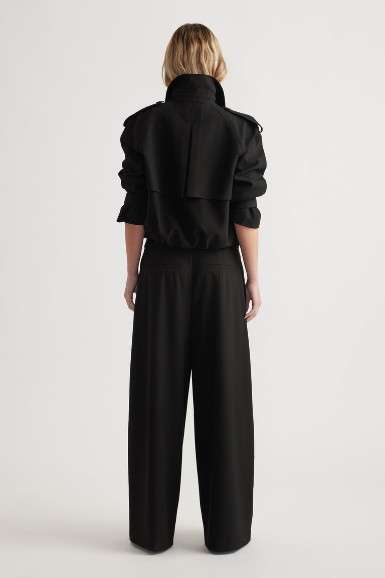 Rear view of woman wearing high-rise wide leg black pants paired with a black cropped jacket with rolled sleeves