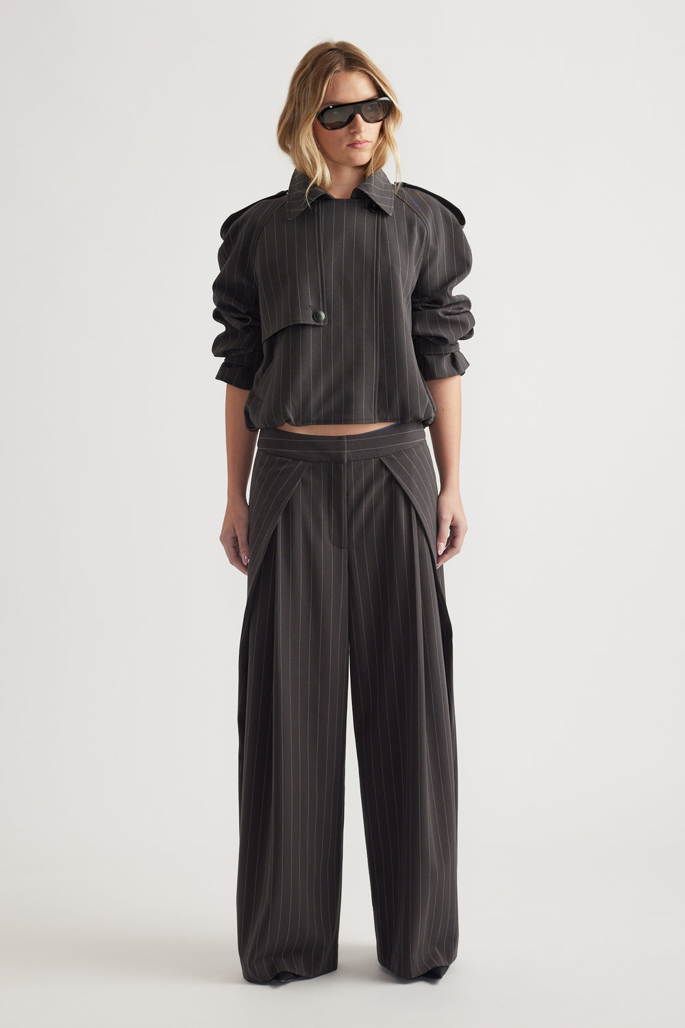 Woman wearing high rise wide leg pinstripe pants with pleat details and a cropped matching jacket and sunglasses
