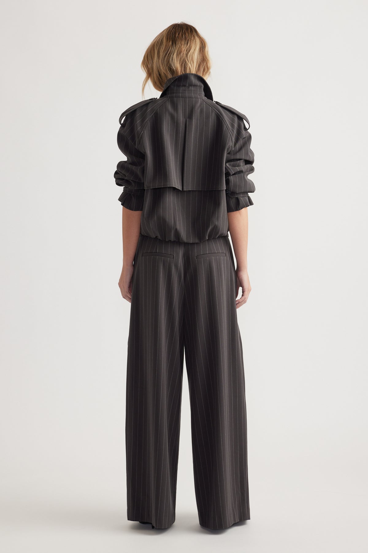 Rear view of woman wearing high-waisted wide leg pinstripe pants paired with a matching long-sleeve top with rolled sleeves