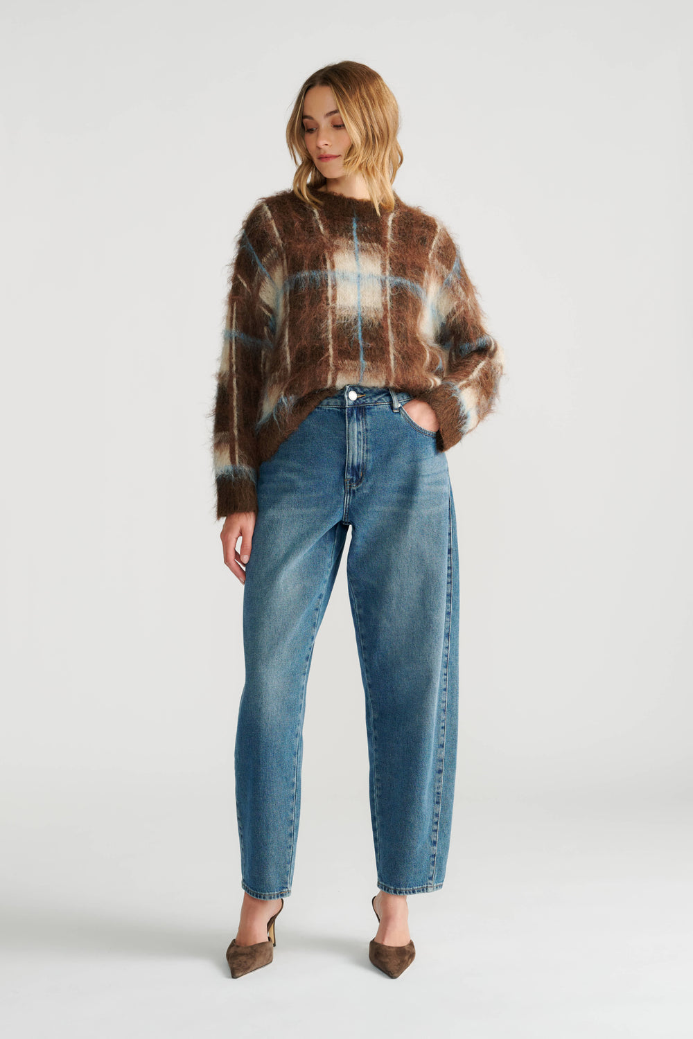 Woman wearing a soft brown plaid knit jumper paired with relaxed blue jeans and brown pointed heels.
