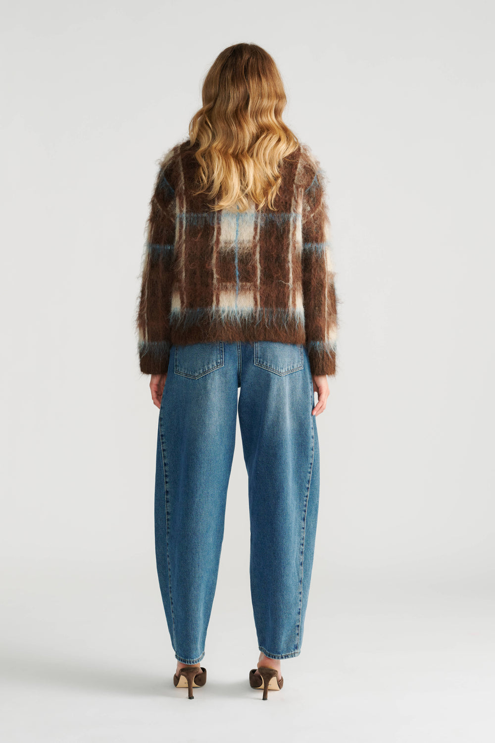 Woman wearing a fuzzy brown check knit jumper paired with relaxed-fit blue denim jeans and heeled shoes, back view.