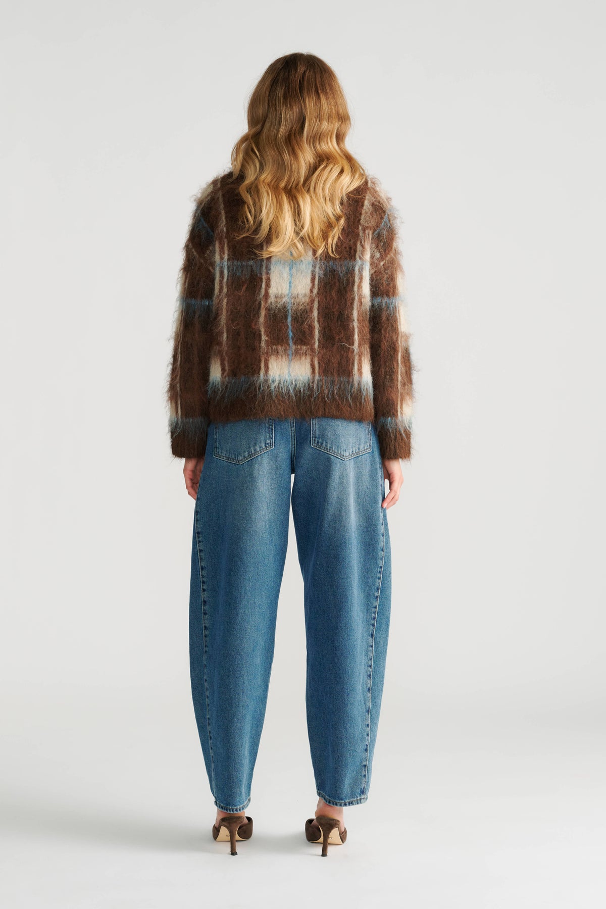 Woman wearing a fuzzy brown check knit jumper paired with relaxed-fit blue denim jeans and heeled shoes, back view.