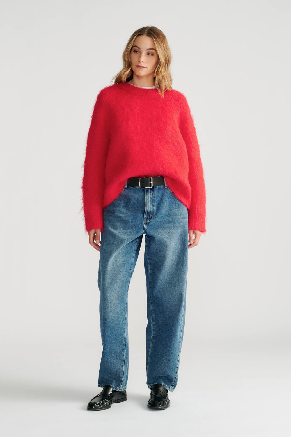 Woman wearing a vibrant red fuzzy knit jumper styled with relaxed straight-leg jeans and black leather loafers.