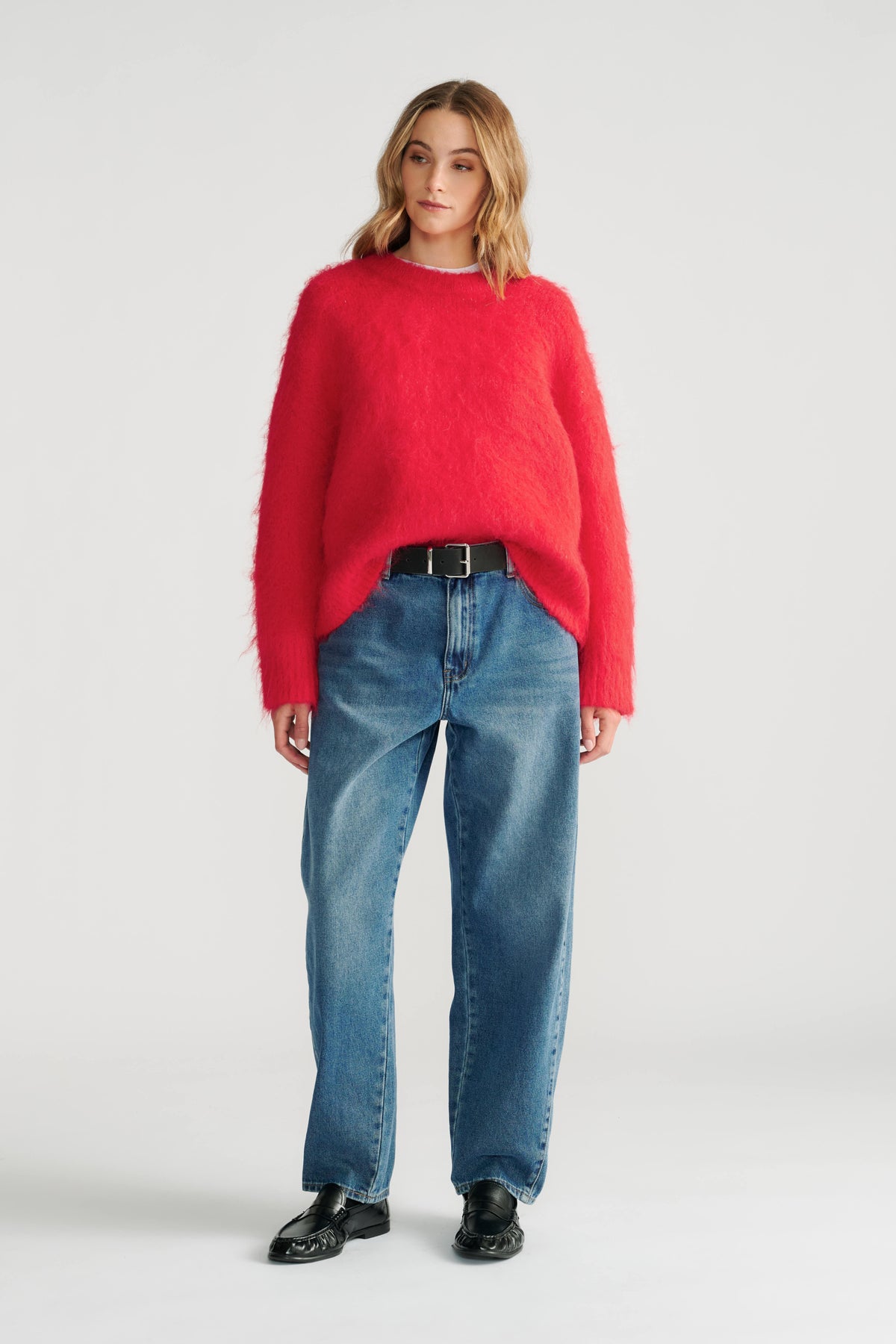 Woman wearing a vibrant red fuzzy knit jumper styled with relaxed straight-leg jeans and black leather loafers.