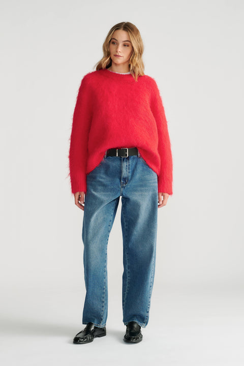 Woman wearing a vibrant red fuzzy knit jumper styled with relaxed straight-leg jeans and black leather loafers.