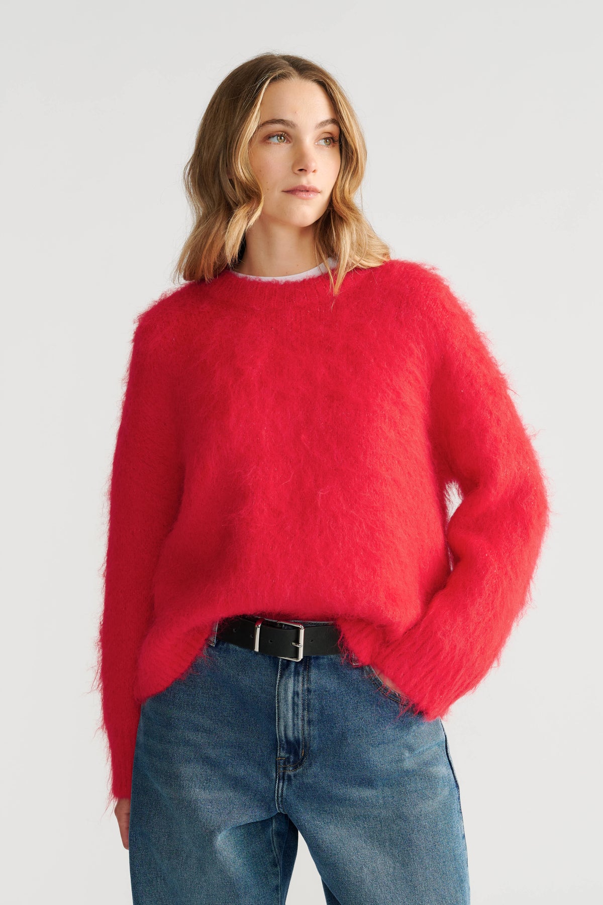 Woman wearing a vibrant red fuzzy knit jumper paired with relaxed blue high-rise jeans and a black belt.