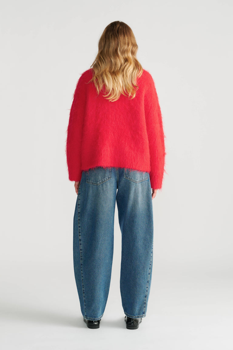 Woman wearing a vibrant red fuzzy knit jumper paired with relaxed fit blue jeans and black shoes, back view.
