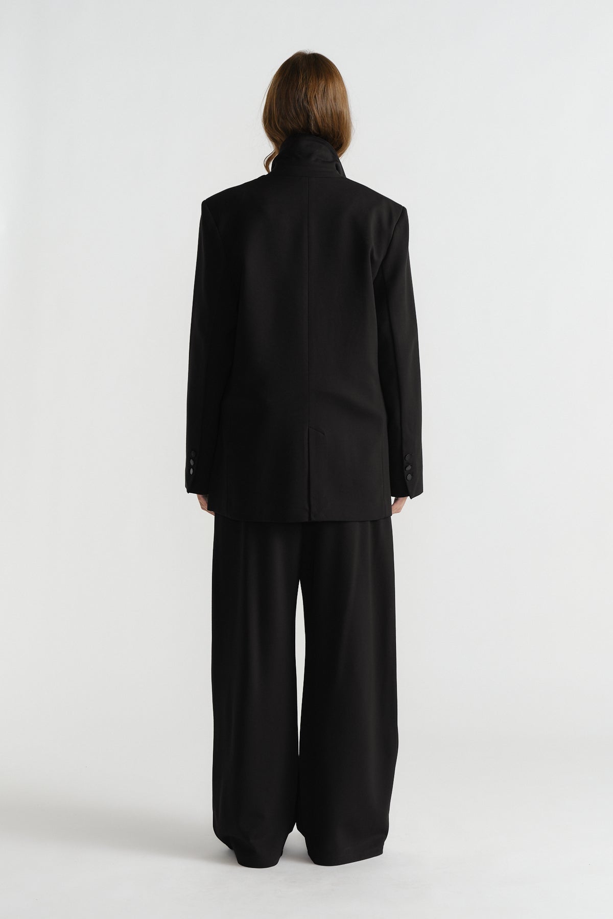 Back view of a woman wearing a structured black blazer with padded shoulders and matching wide-leg trousers