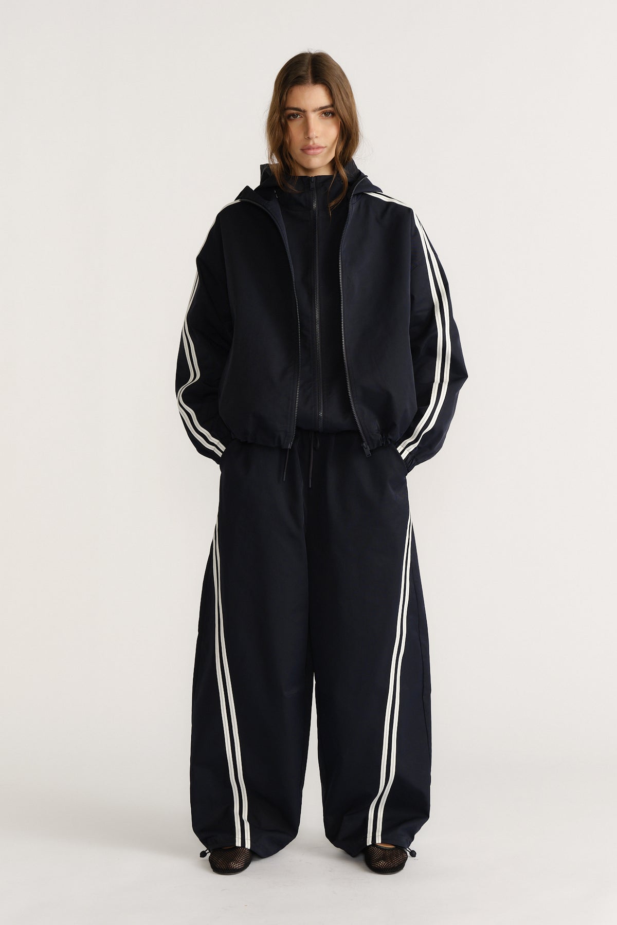 Model wearing navy relaxed fit pants with white side stripes paired with a matching sporty zip-up jacket for a chic casual look