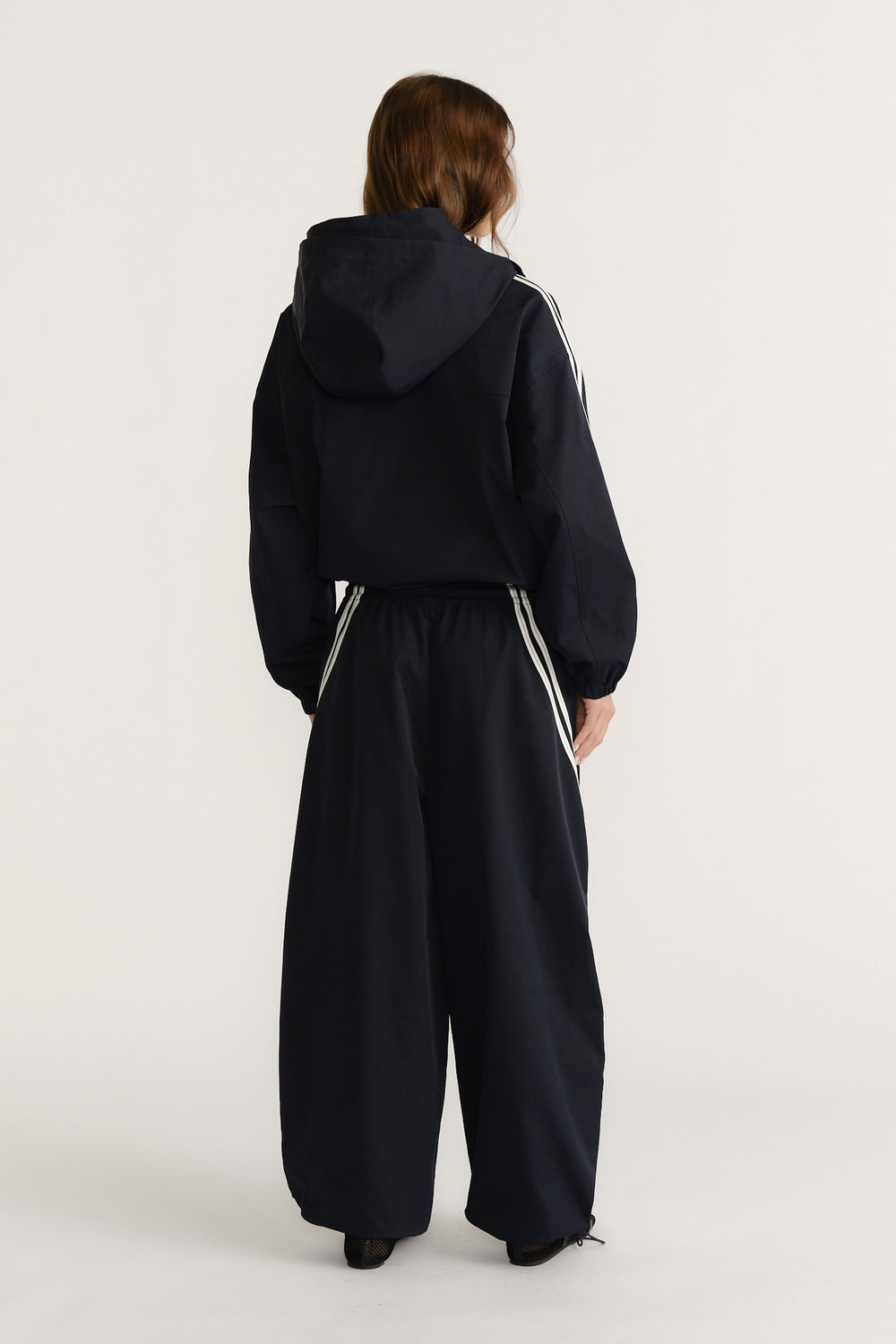 Woman viewed from behind wearing a navy hooded jacket and matching wide-leg pants with white side stripes for a casual look
