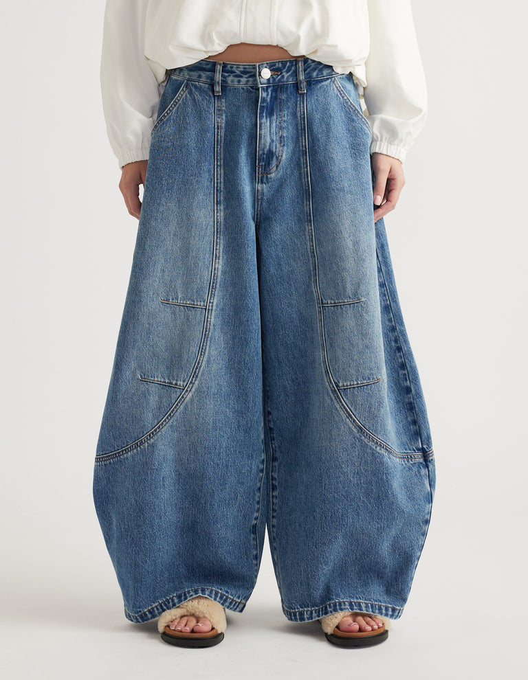 Wide-leg high-rise blue denim jeans with front patch pockets and detailed seam accents worn with sandals and white blouse