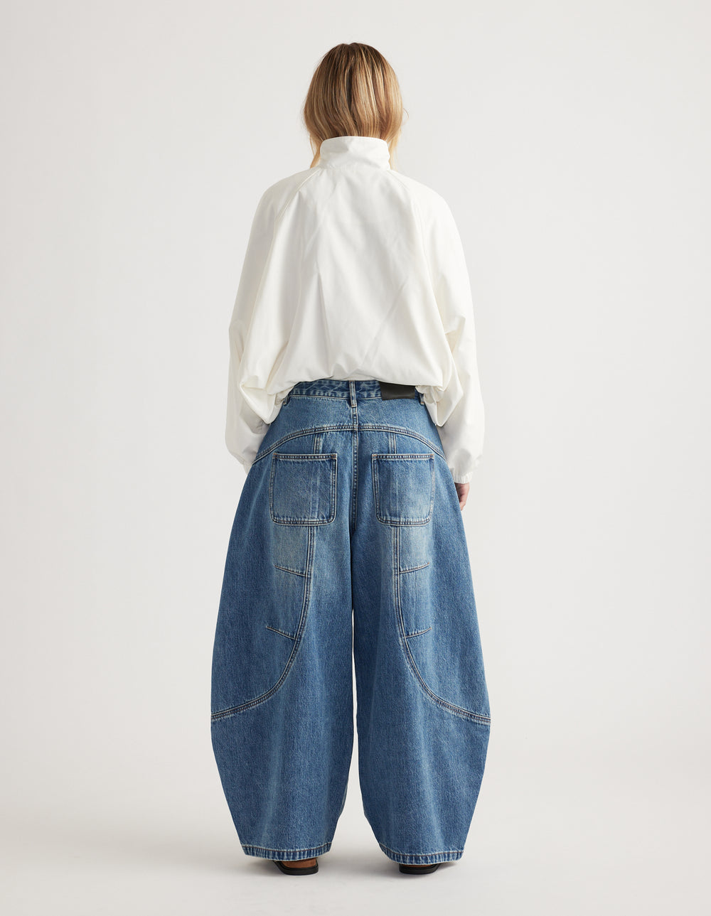 Woman wearing loose wide-leg blue denim jeans with curved seam details and back patch pockets, paired with white top.