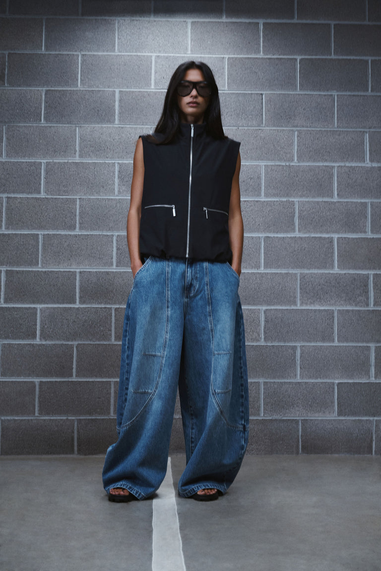Woman wearing blue horseshoe jeans with a black sleeveless zip vest and sunglasses