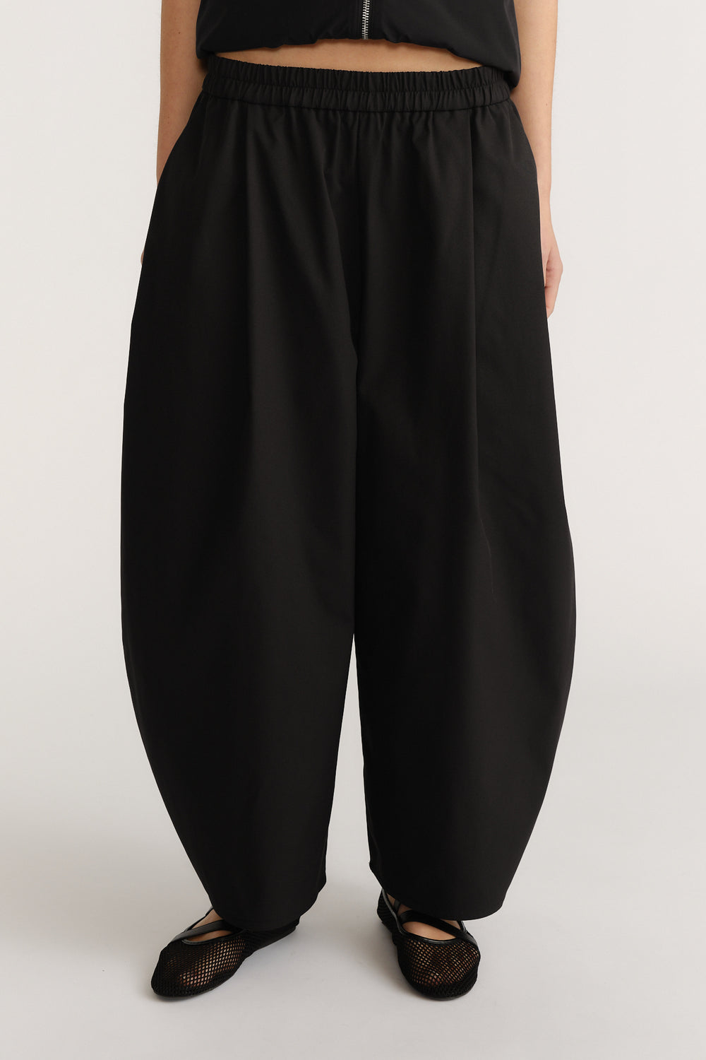 Woman wearing loose black barrel-leg pants with elasticated waist and soft drape paired with mesh flats