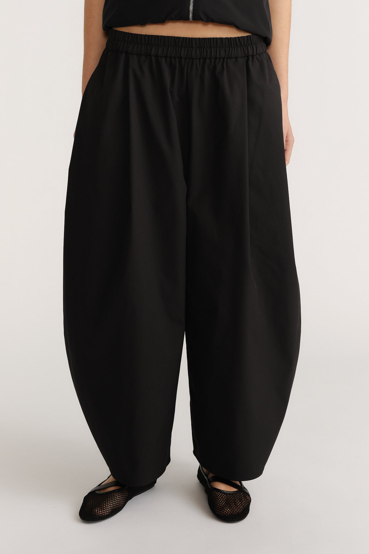 Woman wearing loose black barrel-leg pants with elasticated waist and soft drape paired with mesh flats