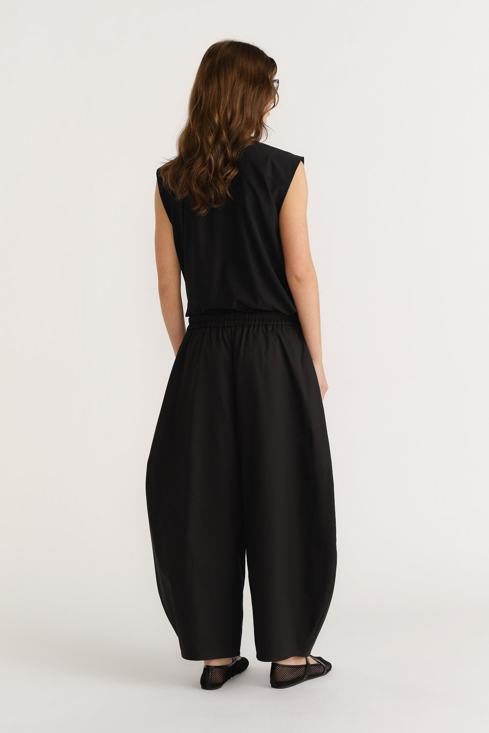 Woman wearing loose black barrel-leg pants with elasticated waist paired with a sleeveless black top and flats