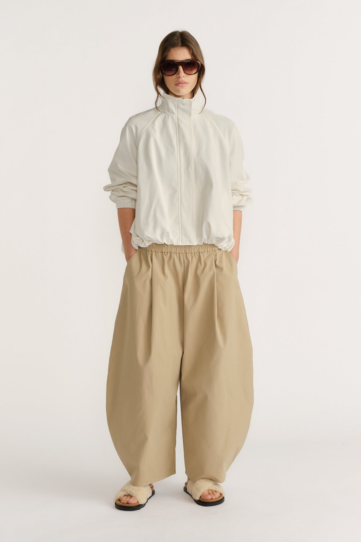 Woman wearing oversized beige barrel pants paired with a loose white jacket and sunglasses for a relaxed look.
