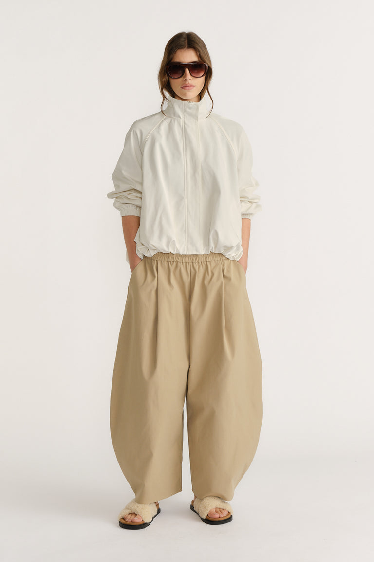 Woman wearing oversized beige barrel pants paired with a loose white jacket and sunglasses for a relaxed look.
