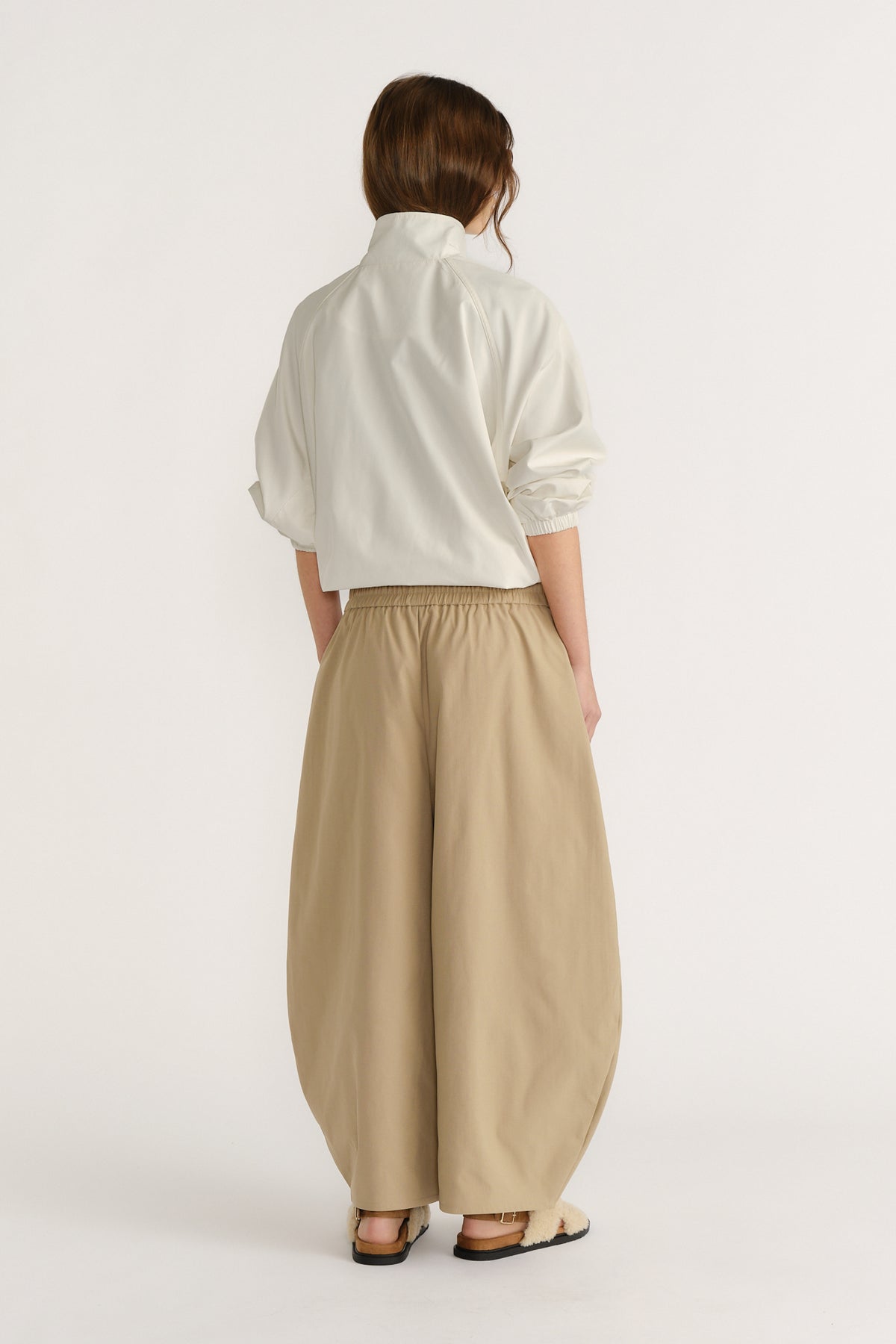Woman wearing loose, wide-legged beige pants with an elastic waist paired with a cropped white top and sandals
