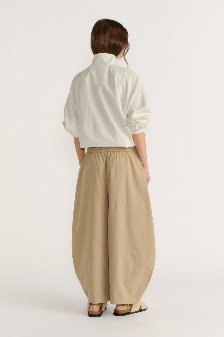 Woman wearing loose, wide-legged beige pants with an elastic waist paired with a cropped white top and sandals